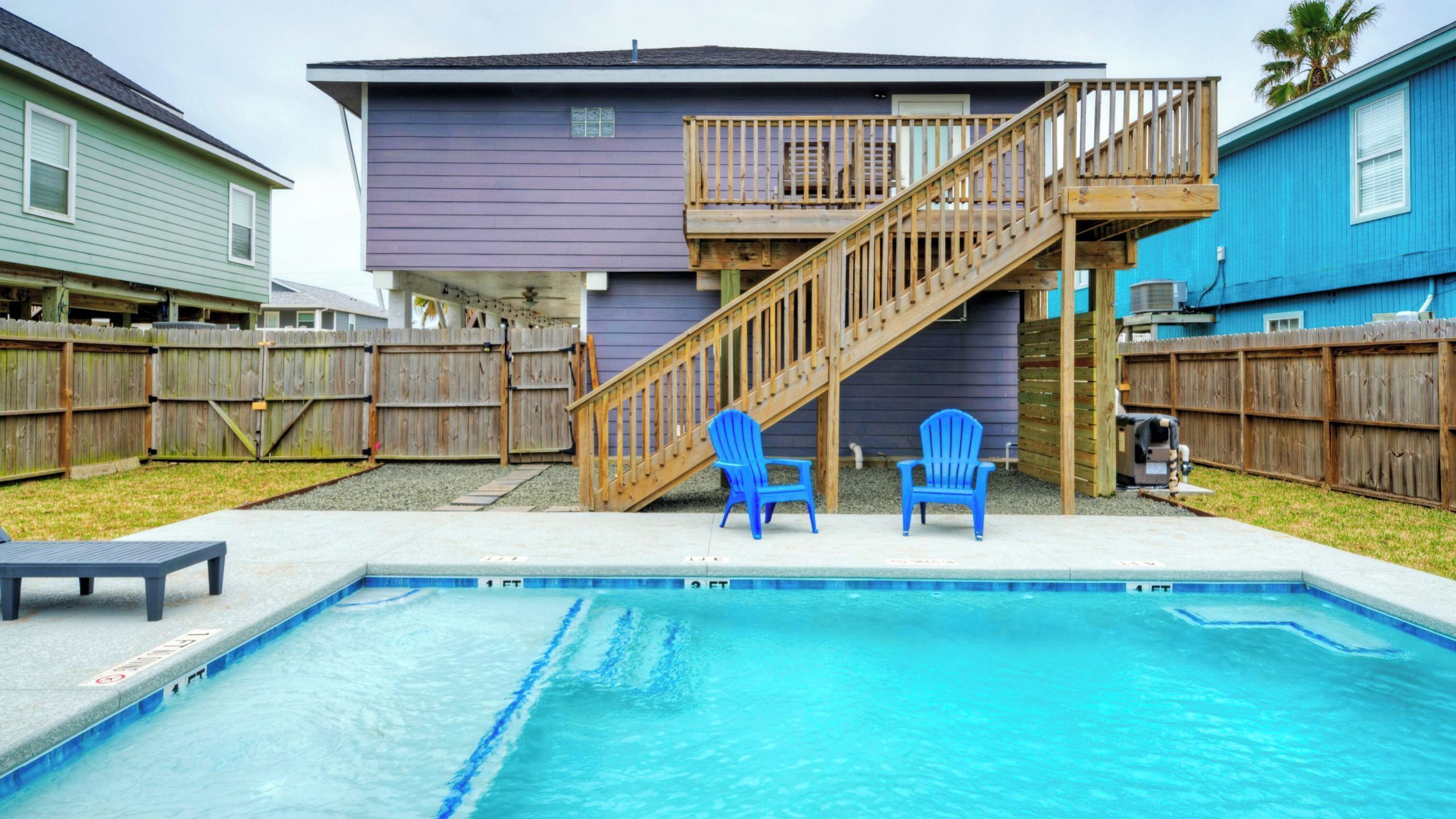 A backyard with a swimming pool, wooden deck, and two blue chairs.