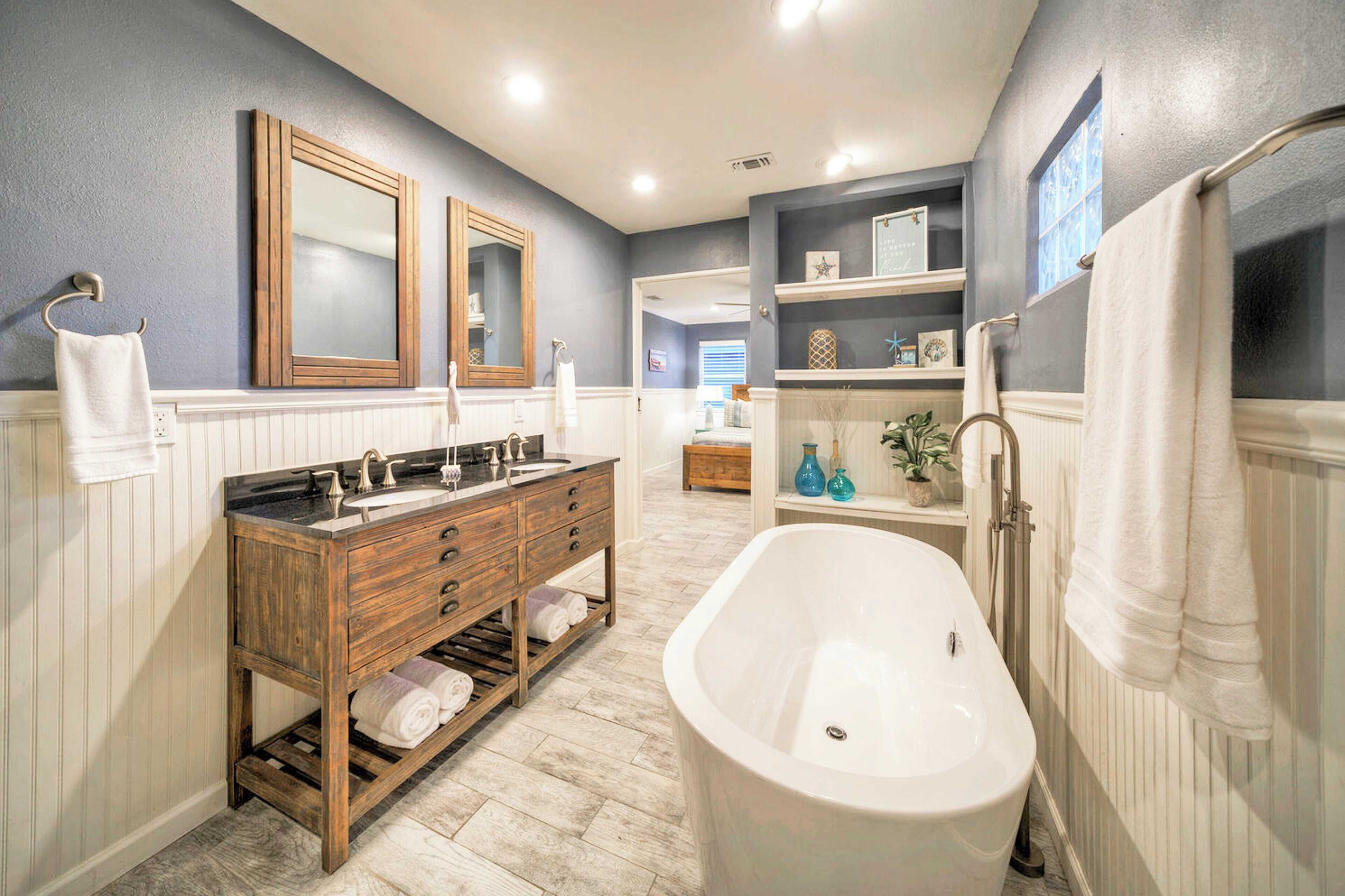 A bathroom with a freestanding bathtub, a wooden vanity with a double sink, and a large mirror.
