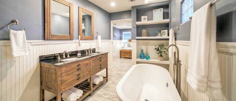 A bathroom with a freestanding bathtub, a wooden vanity with a double sink, and a large mirror.