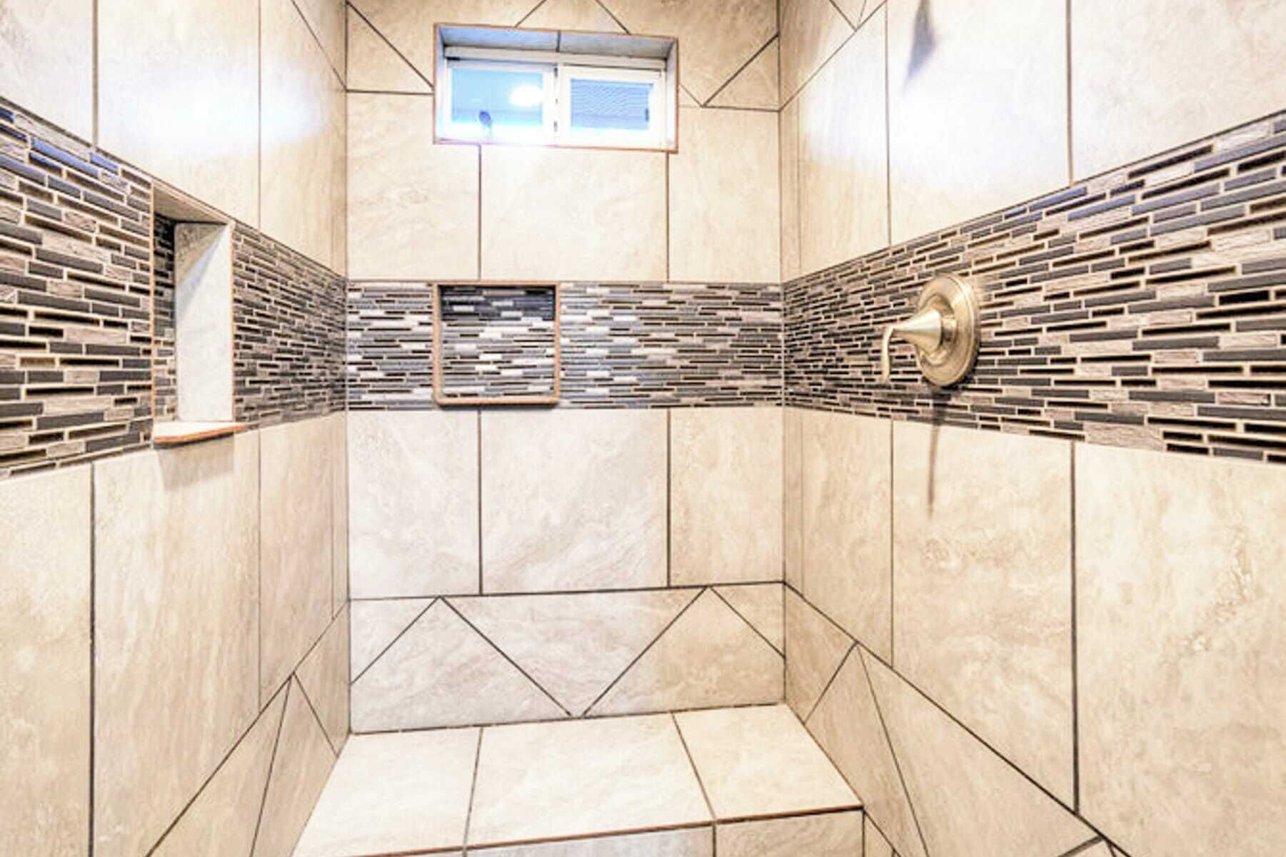 Een moderne douche met geometrische tegelpatronen en een inbouwkastje.