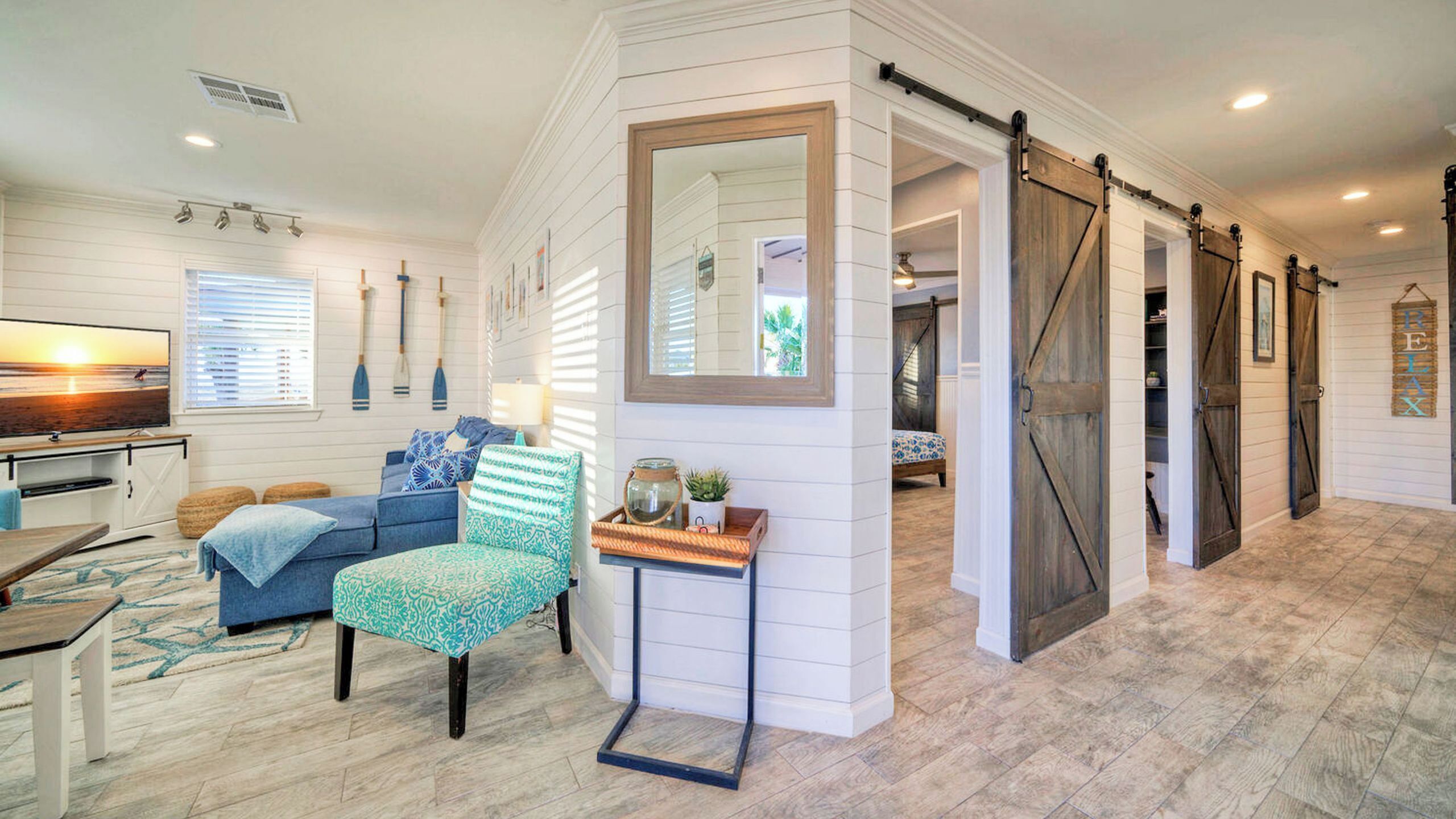 A room with a large mirror, a sliding barn door, a sofa, a chair, and a small table with a plant.