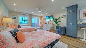 Una camera d'albergo con due letti, una televisione, un ventilatore a soffitto e un'ampia finestra.