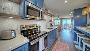 A modern kitchen with a built-in oven, microwave, and toaster, a large window, and a seating area with bar stools. - Ocean View w/ Pool, Tennis/pickleball, Beach Access Summer Love by Avantstay (Port Aransas)