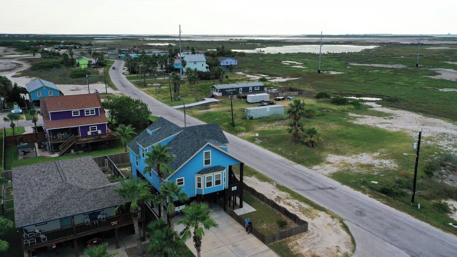 A coastal residential area with houses, a road, and a beach in the background.