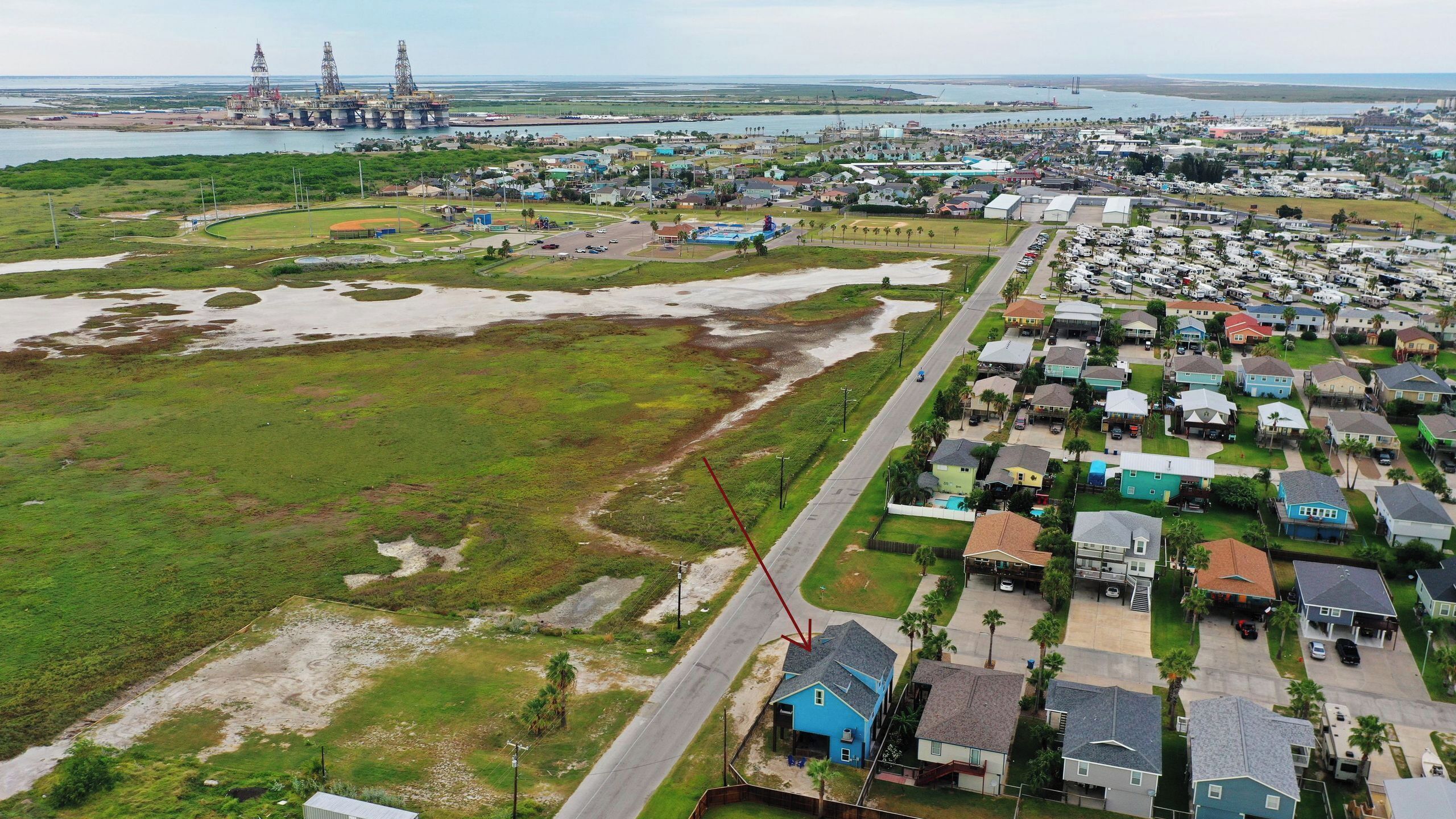 Vue aérienne d’un quartier résidentiel situé sur la côte, avec des maisons, une route et, au loin, des bâtiments industriels.