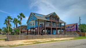 A two-story house with a balcony, wooden deck, and a fenced yard. - Incredible Nature Views, Golf Cart for Rent, Balcony Blue Crush by Avantstay (Port Aransas)