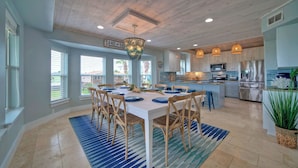 A spacious kitchen with a dining area, wooden ceiling, and large windows.