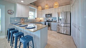 A modern kitchen with white cabinets, a large island with bar stools, stainless steel appliances, and pendant lighting.