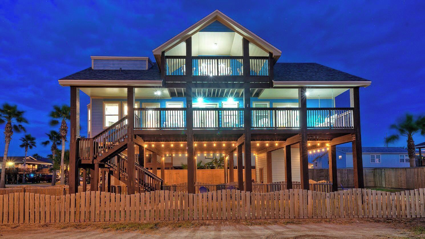 Une maison à deux étages dotée d’un balcon, d’une terrasse en bois et de guirlandes lumineuses.