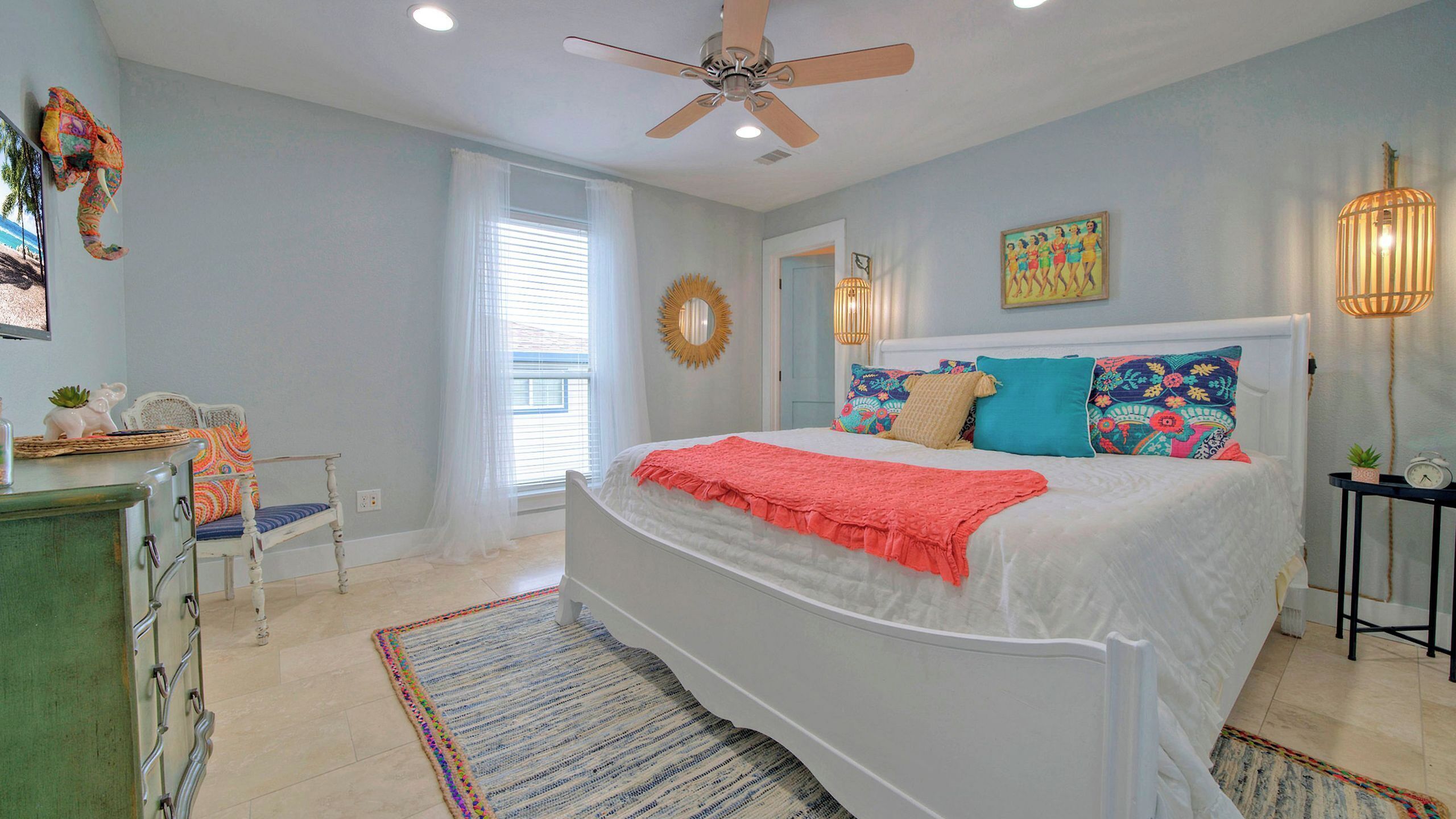 A bedroom with a bed, a dresser, a chair, a ceiling fan, a window, and a painting on the wall.