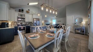 A modern kitchen with white cabinetry, a central island, and a dining area with white chairs. - Peachy Palm by Avantstay Huge Private Pool! (Port Aransas)