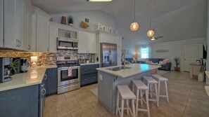 A modern kitchen with white cabinets, a large island with stools, a microwave, oven, and refrigerator. - Peachy Palm by Avantstay Huge Private Pool! (Port Aransas)