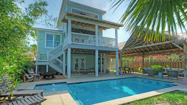 Uma casa de dois andares com piscina, móveis de exterior e um alpendre coberto.
