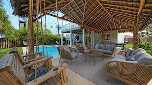 A covered outdoor seating area with wooden furniture, a pool, and a house in the background. - Beach Access Private Pool, Ping-pong, Firepit, Swings, & Views Tipsea Turtle (Port Aransas)