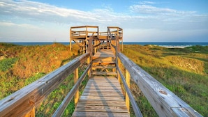 A wooden boardwalk leading to a wooden structure, surrounded by grassy dunes and the ocean. - Beach Access Private Pool, Ping-pong, Firepit, Swings, & Views Tipsea Turtle (Port Aransas)