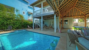 Uma área de piscina com deck de madeira, espreguiçadeiras e um espaço de estar coberto.
