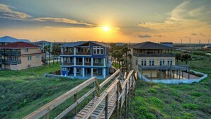 A coastal residential area with multi-story houses, a wooden boardwalk, and a sunset in the background. - Beach Access Private Pool, Ping-pong, Firepit, Swings, & Views Tipsea Turtle (Port Aransas)