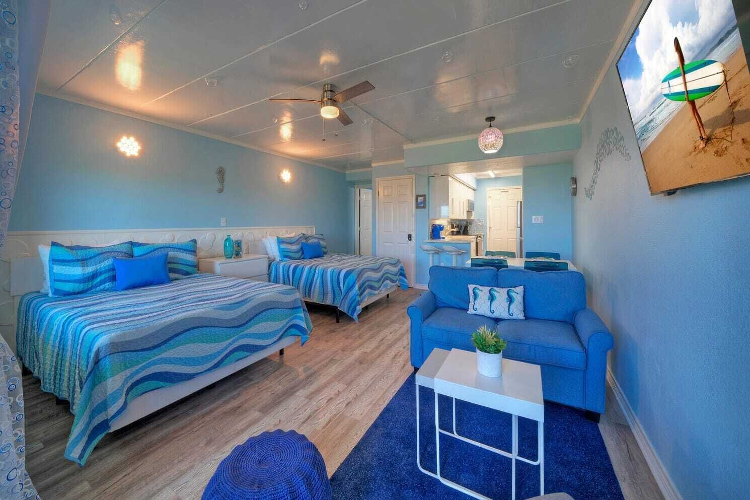 Une chambre avec deux lits, un canapé bleu, une petite table et un ventilateur de plafond.