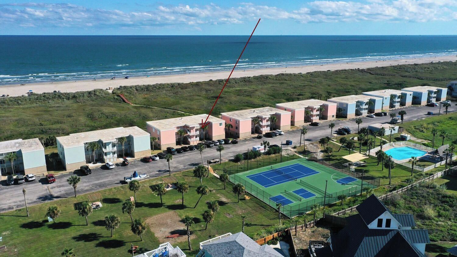 A coastal hotel with multiple buildings, a tennis court, and a beach view.