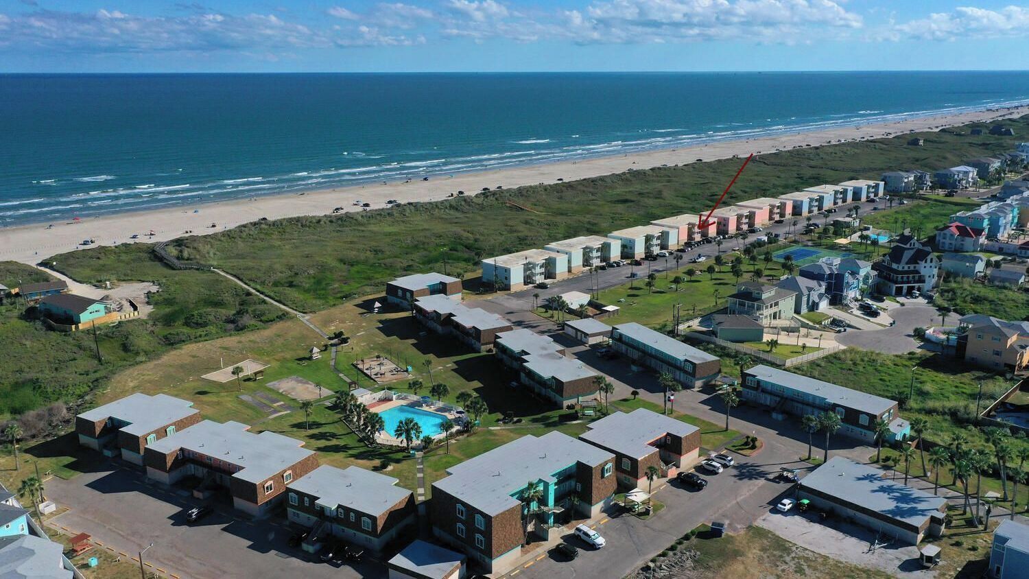 An aerial view of a coastal hotel with multiple buildings, a swimming pool, and a beach in the background.