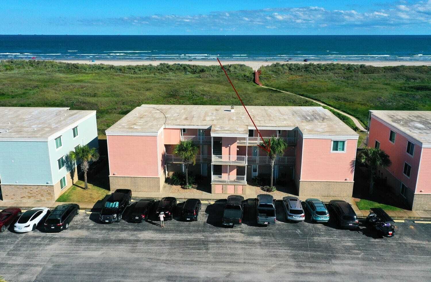 Een meerhoog gebouw met een parkeerplaats ervoor, uitkijkend over een strand.