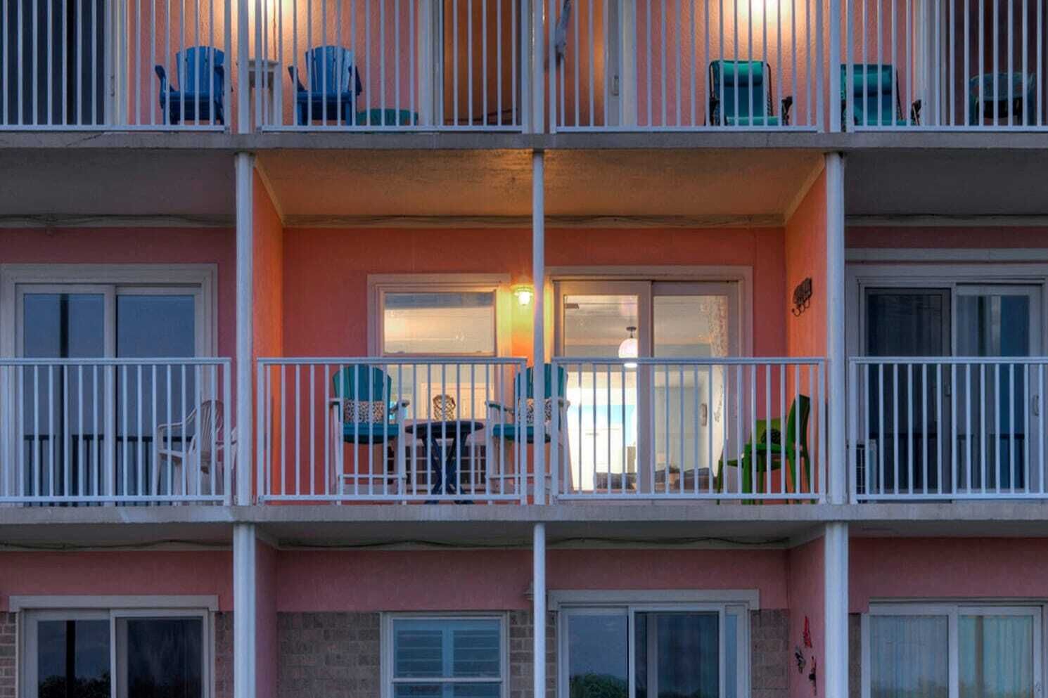 A multi-story building with balconies, each featuring white railings and outdoor seating.