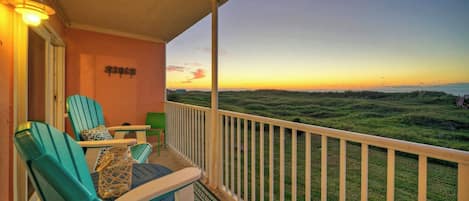 A balcony with chairs and a table, a view of the landscape, and a sunset.