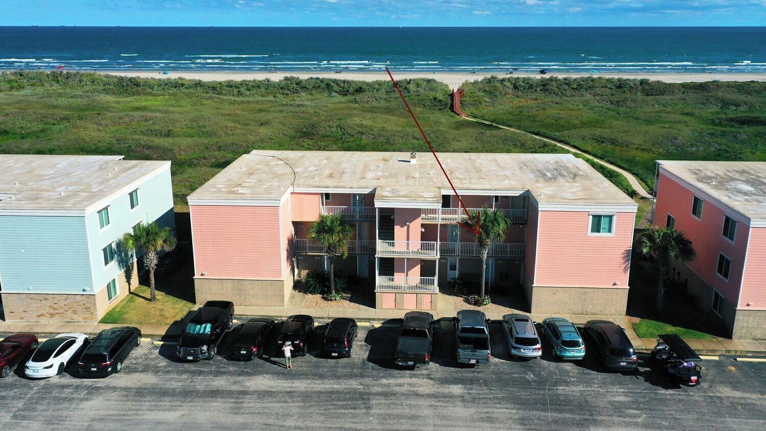 A beachfront property with a parking lot, a building with a balcony, and a view of the ocean.