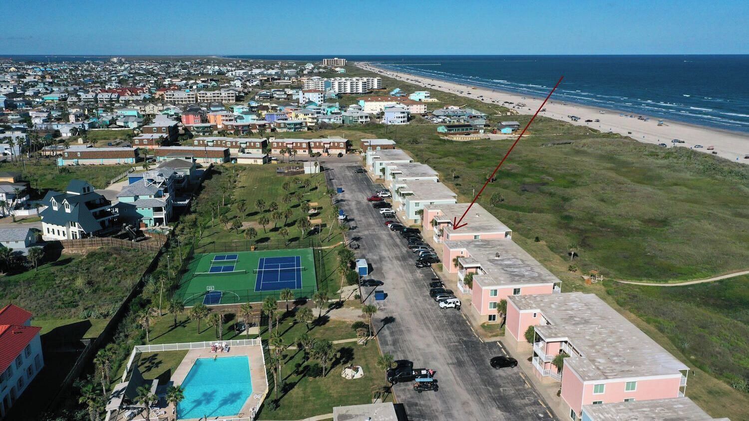 An aerial view of a coastal residential area with houses, a tennis court, and a swimming pool.