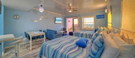 Una habitación de hotel con cama, escritorio, silla, televisor y balcón con vistas.