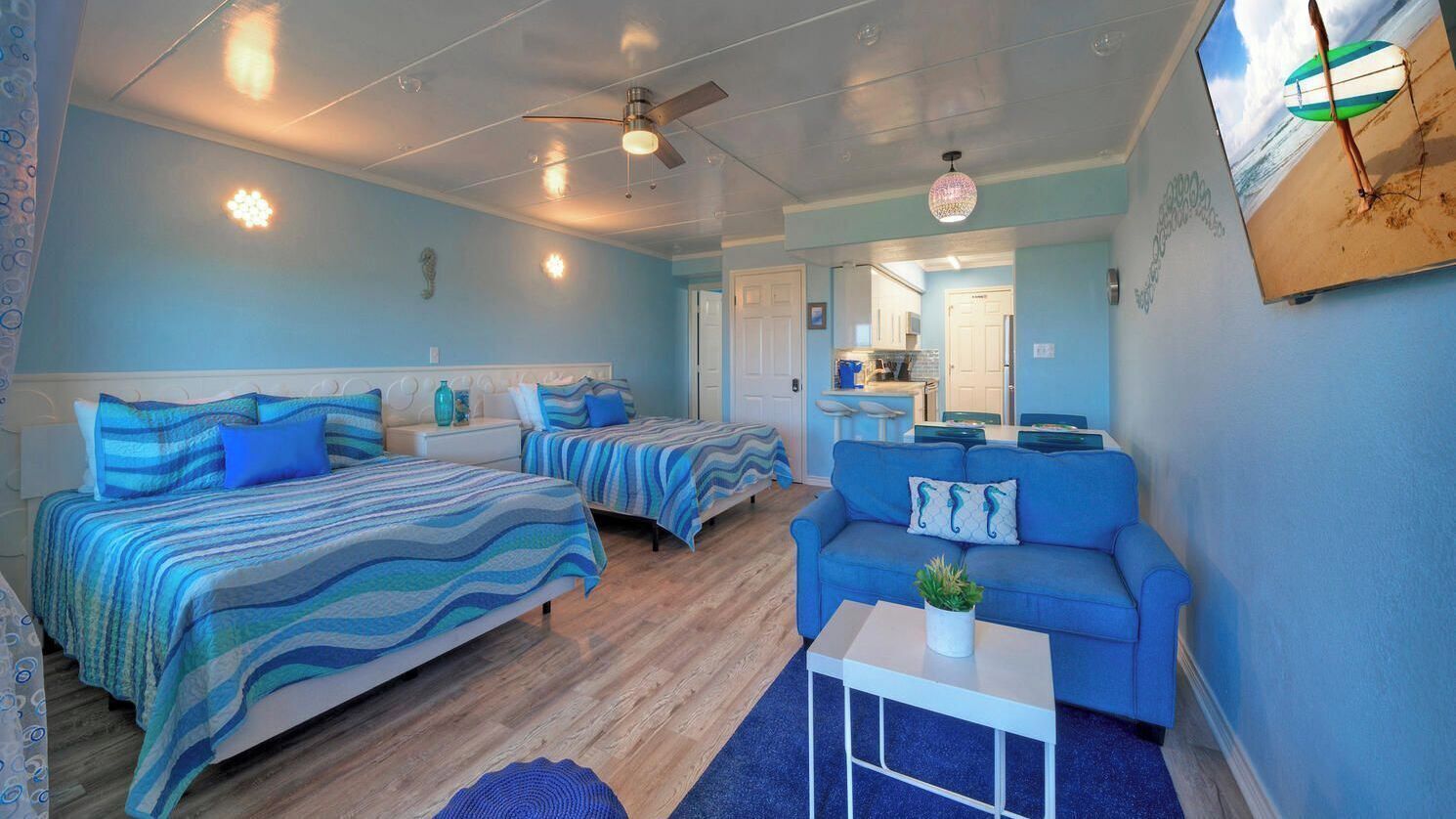 A bedroom with two beds, a blue sofa, a small table, and a ceiling fan.