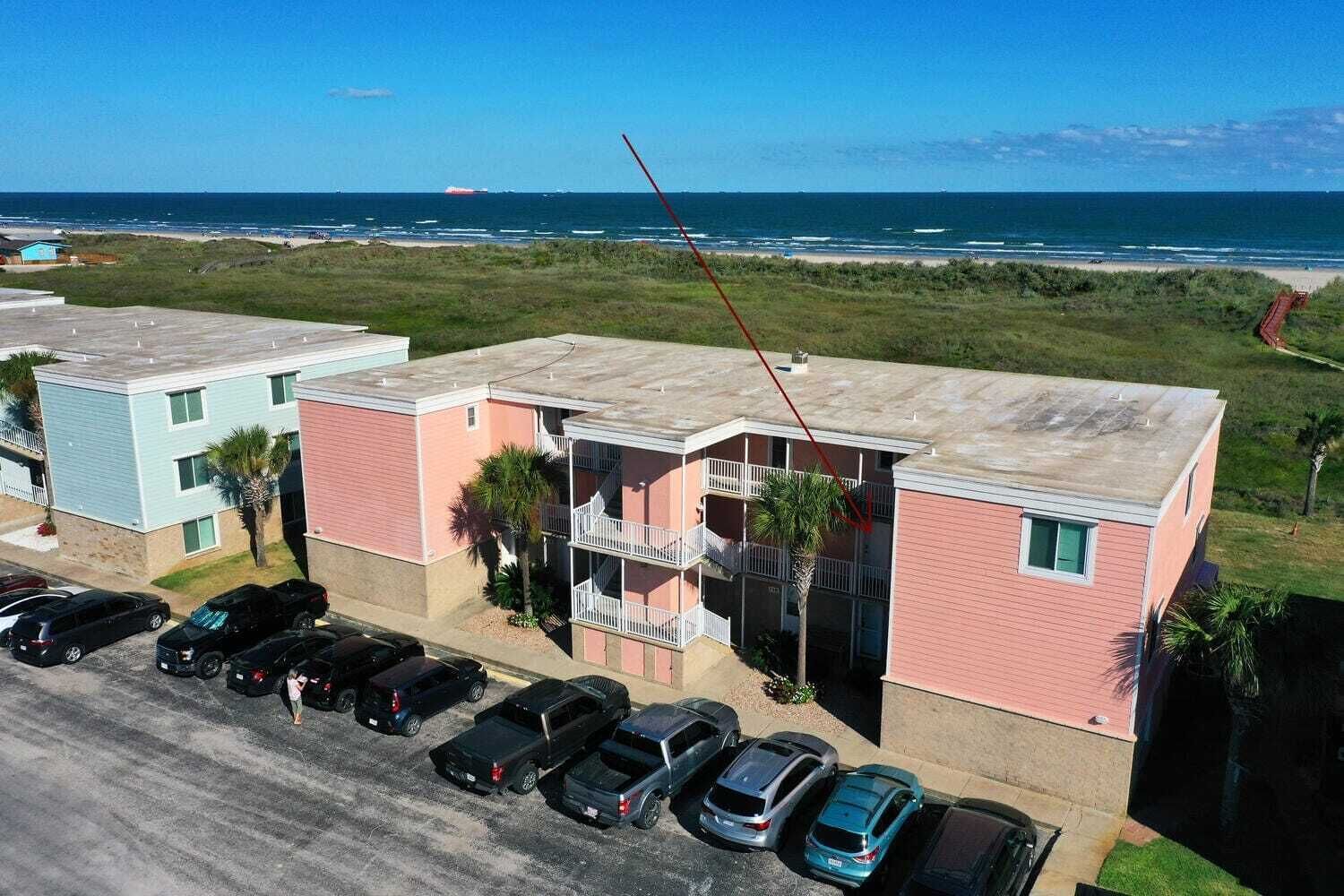 Un edificio de varios pisos con un estacionamiento al frente, cerca de la playa.