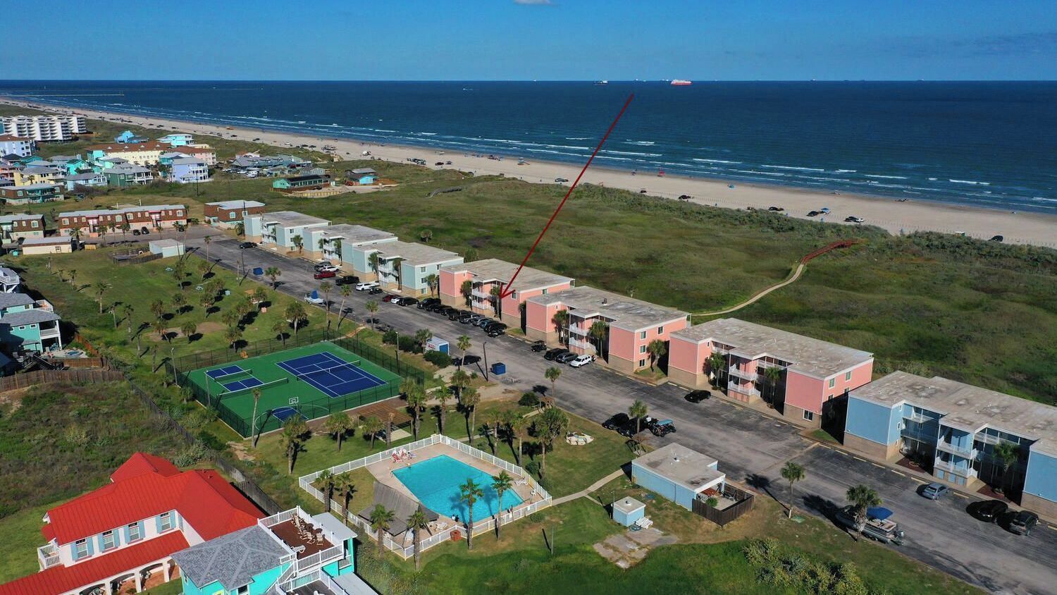 A coastal residential area with a beach, a tennis court, and a swimming pool.