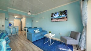 Een kamer met een blauwe bank, een grijze fauteuil, een klein witte tafel, een blauw vloerkleed en wanddecoratie met een strandthema.
