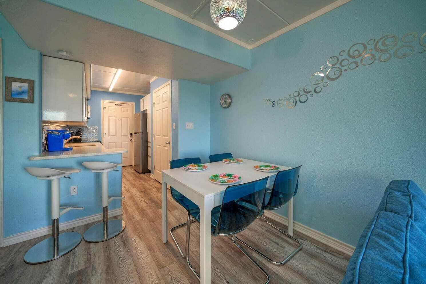 A compact kitchen with a refrigerator, a dining table with chairs, and a blue wall with decorative circles.
