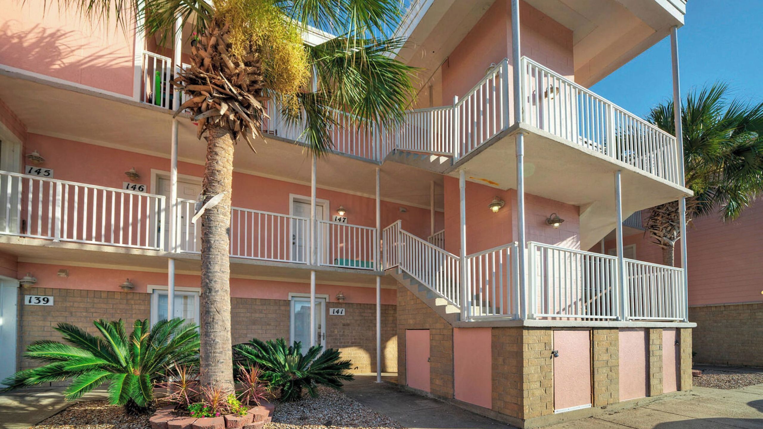 A multi-story hotel with balconies, palm trees, and a brick facade.