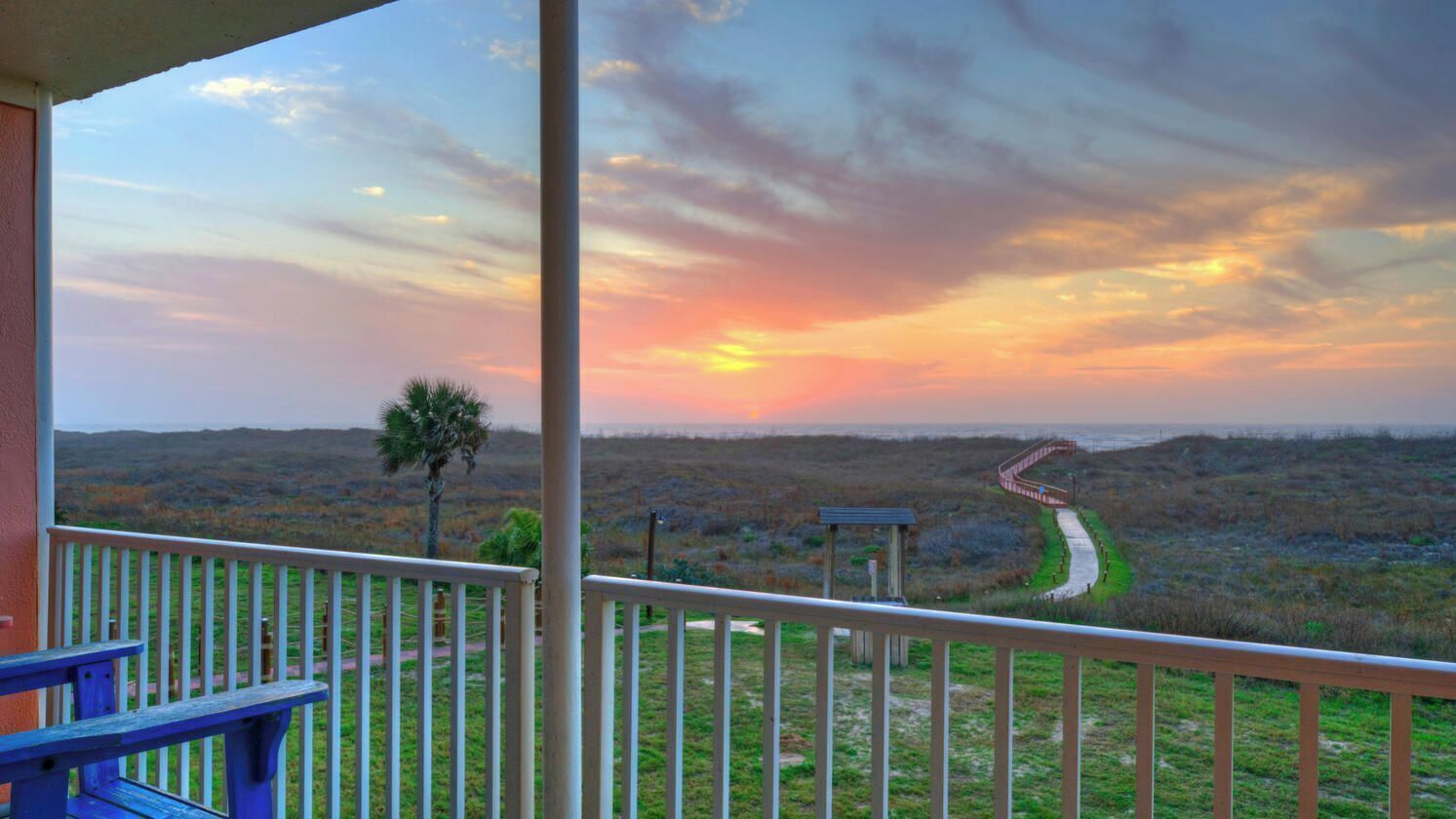 A balcony with a view of a sunset over a landscape with a winding path.