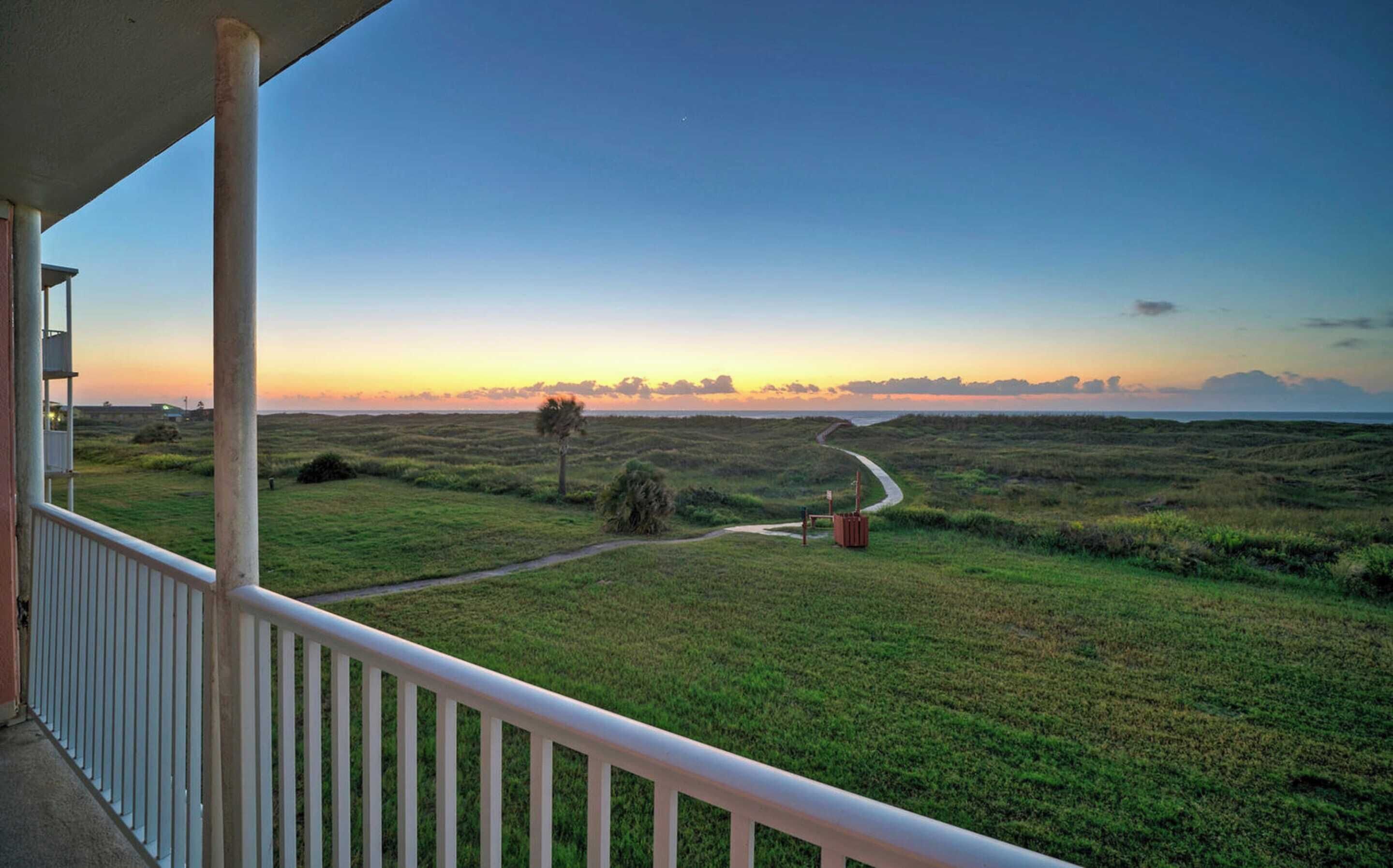 A balcony with a view of a grassy landscape and a sunset.