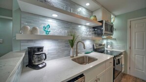 A modern kitchen with a marble countertop, stainless steel sink, built-in oven, and a coffee maker. - Beachfront Condo, Prvt Balcony w/ View, Pool Access Beach Happy by Avantstay (Port Aransas)