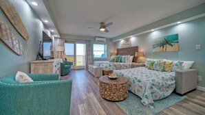 A spacious living area with a sofa, a round coffee table, and a bed with a patterned bedspread. - Beachfront Condo, Prvt Balcony w/ View, Pool Access Beach Happy by Avantstay (Port Aransas)