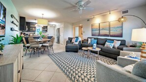 A modern living room with a dining area, grey sofas, a patterned rug, and a ceiling fan. - Beachfront Retreat w/ 2 Pools + Tennis + Bikes + Boardwalk Pura Vida by Avantstay (Port Aransas)