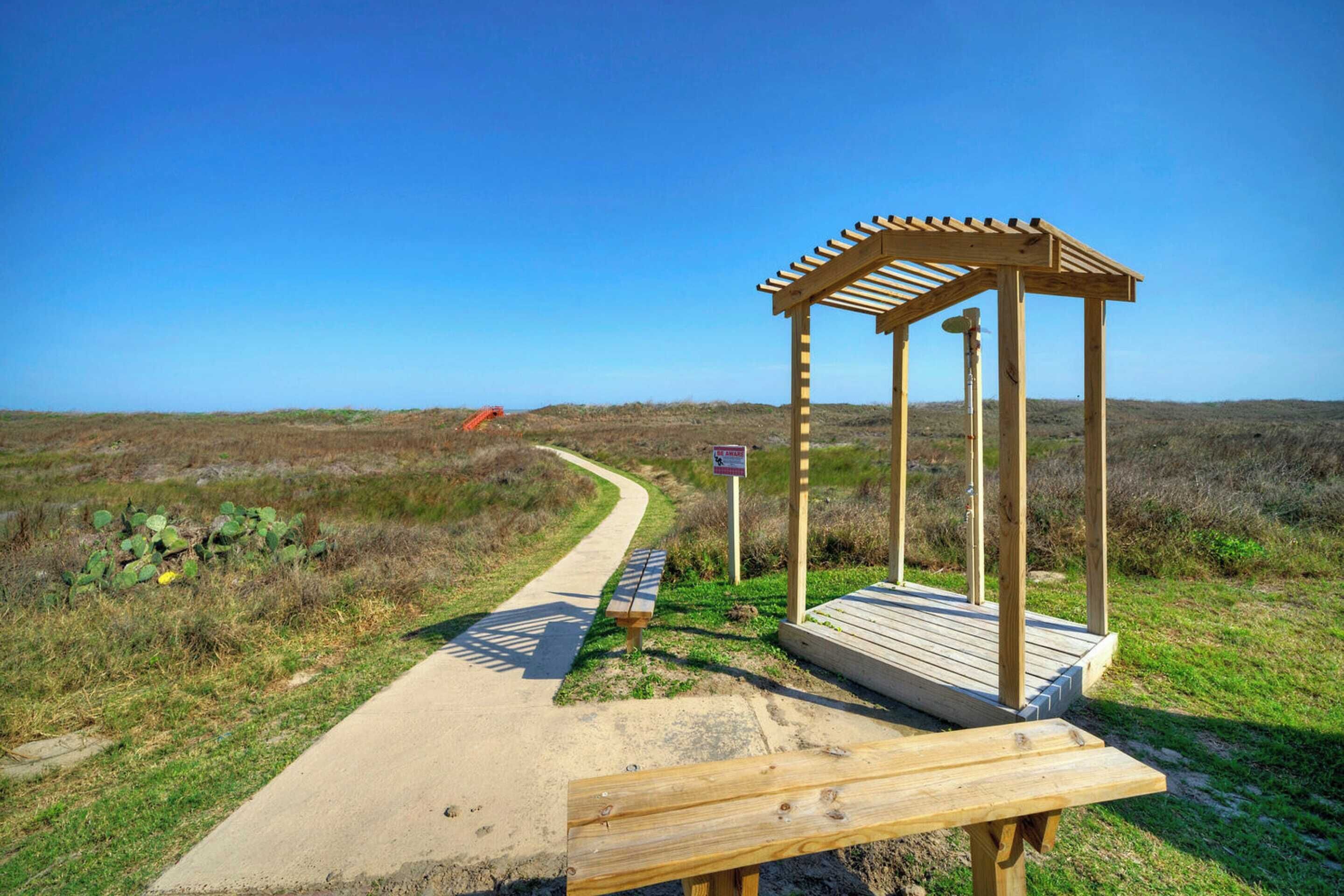 Un kiosque en bois avec un banc, un chemin pavé et un panneau, le tout intégré dans un paysage naturel.