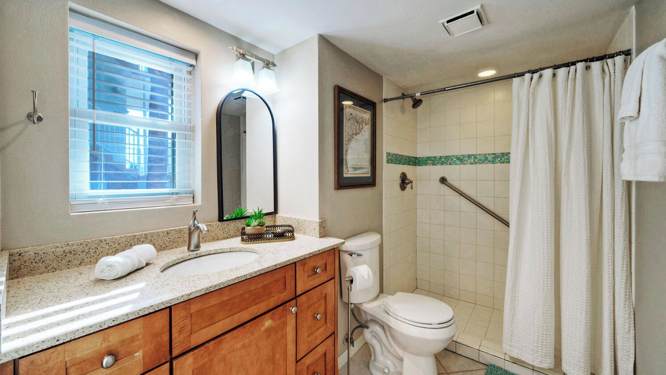 A bathroom with a vanity, toilet, shower, and a window with blinds.