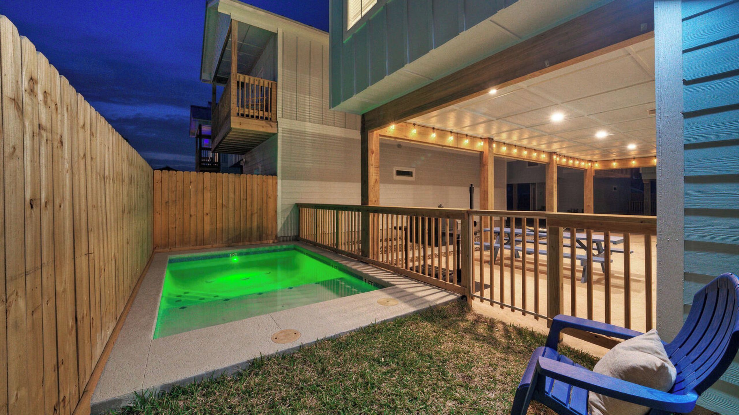 Een achtertuin met een hottub, houten terras en een stoel.