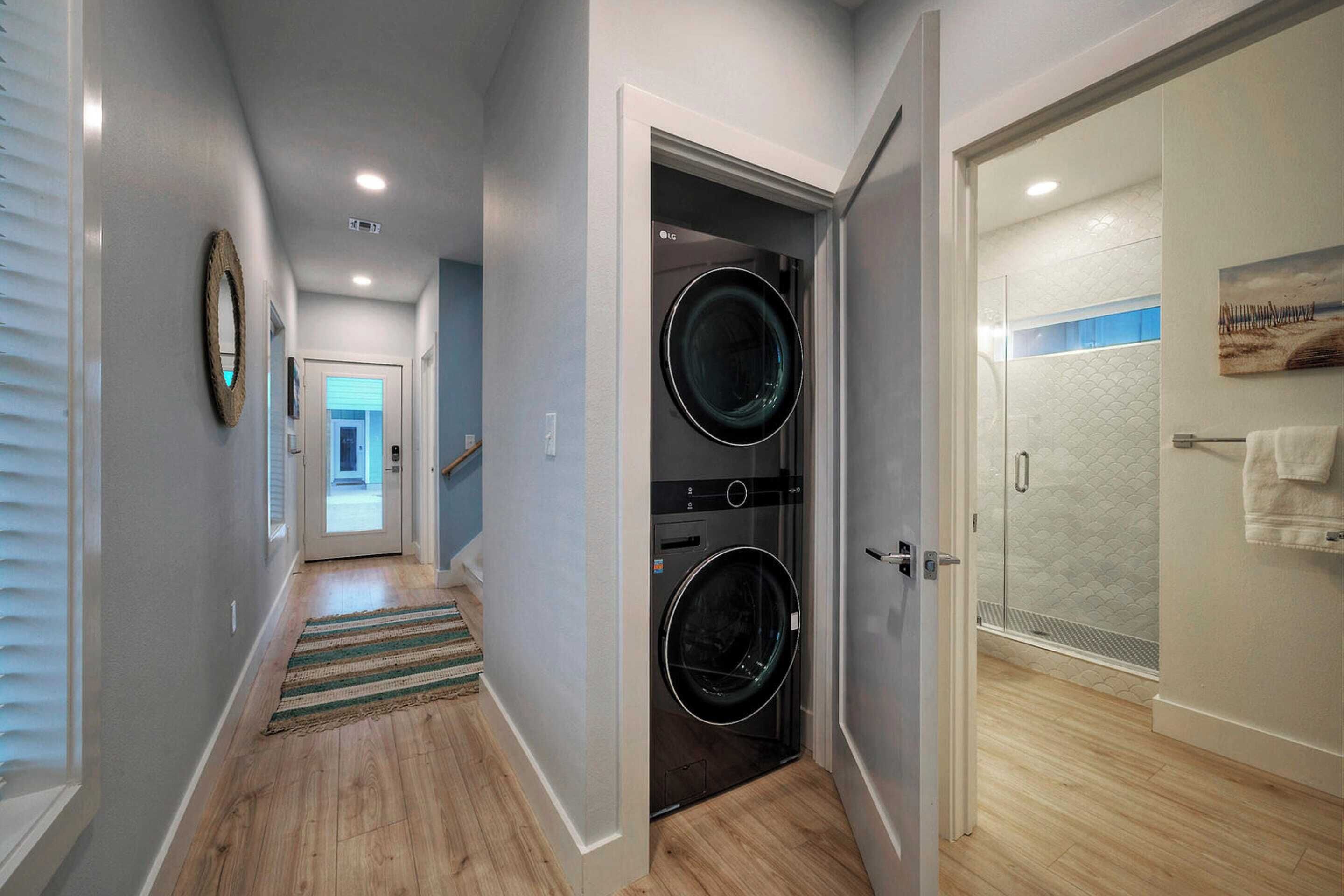 A hallway with a washing machine and dryer, a wooden floor, and a door leading to a bathroom with a towel rack.