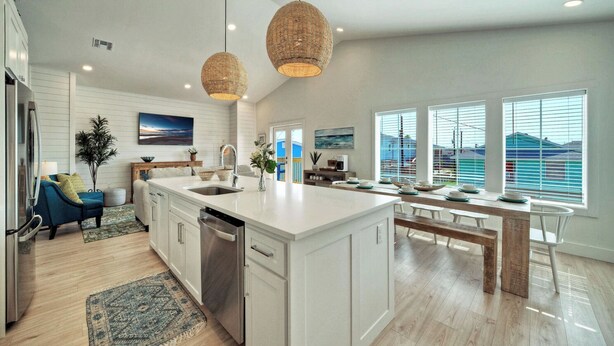 A modern kitchen with a large island, pendant lighting, and a view of the ocean through large windows.