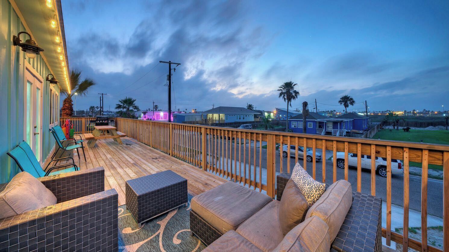 A wooden deck with outdoor seating, a view of the street, and a clear sky.
