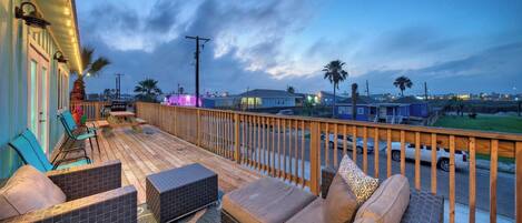 A wooden deck with outdoor seating, a view of the street, and a clear sky.