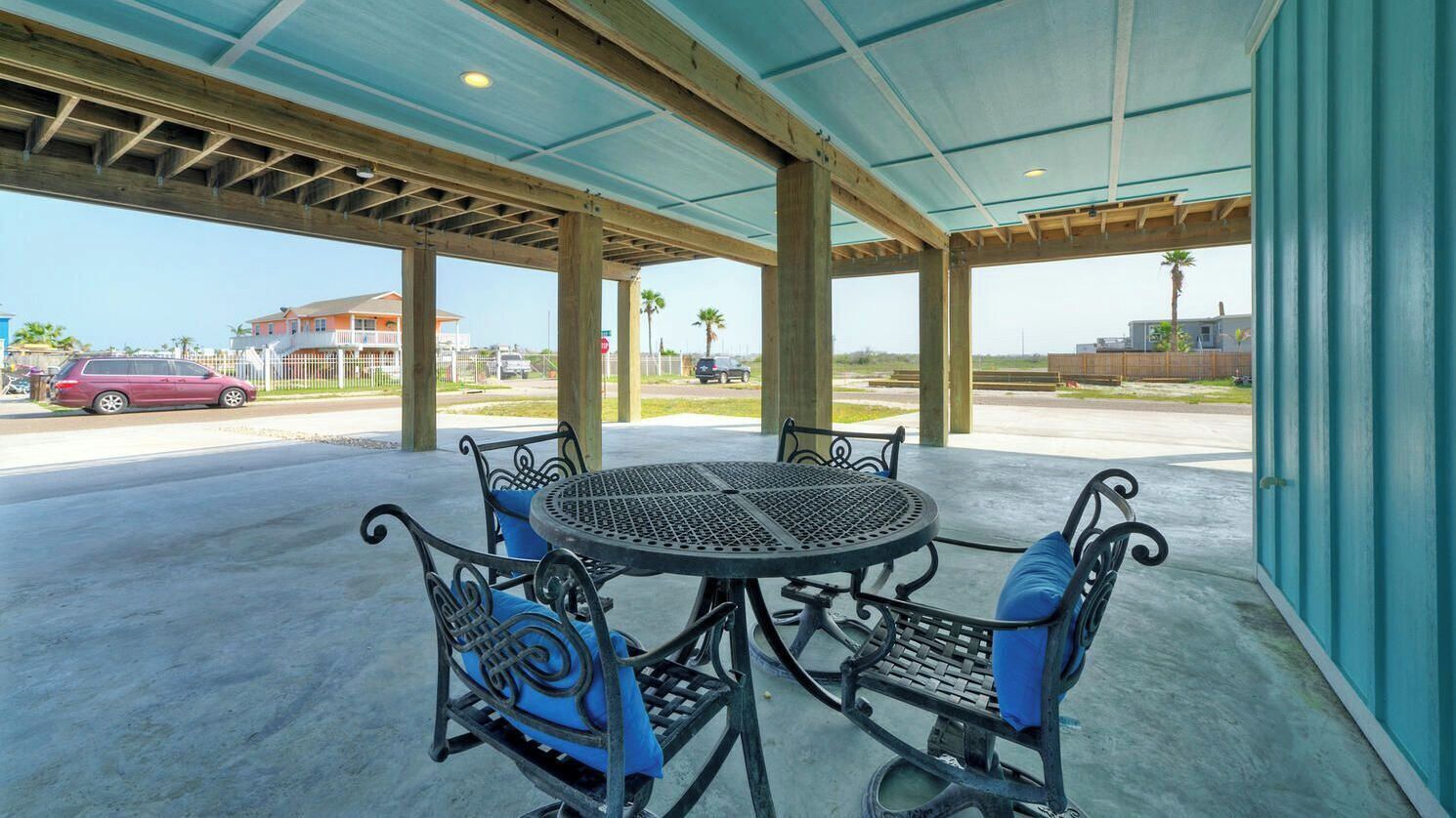 An outdoor covered patio with a round table and four chairs, a concrete floor, and a view of the street and buildings in the background.