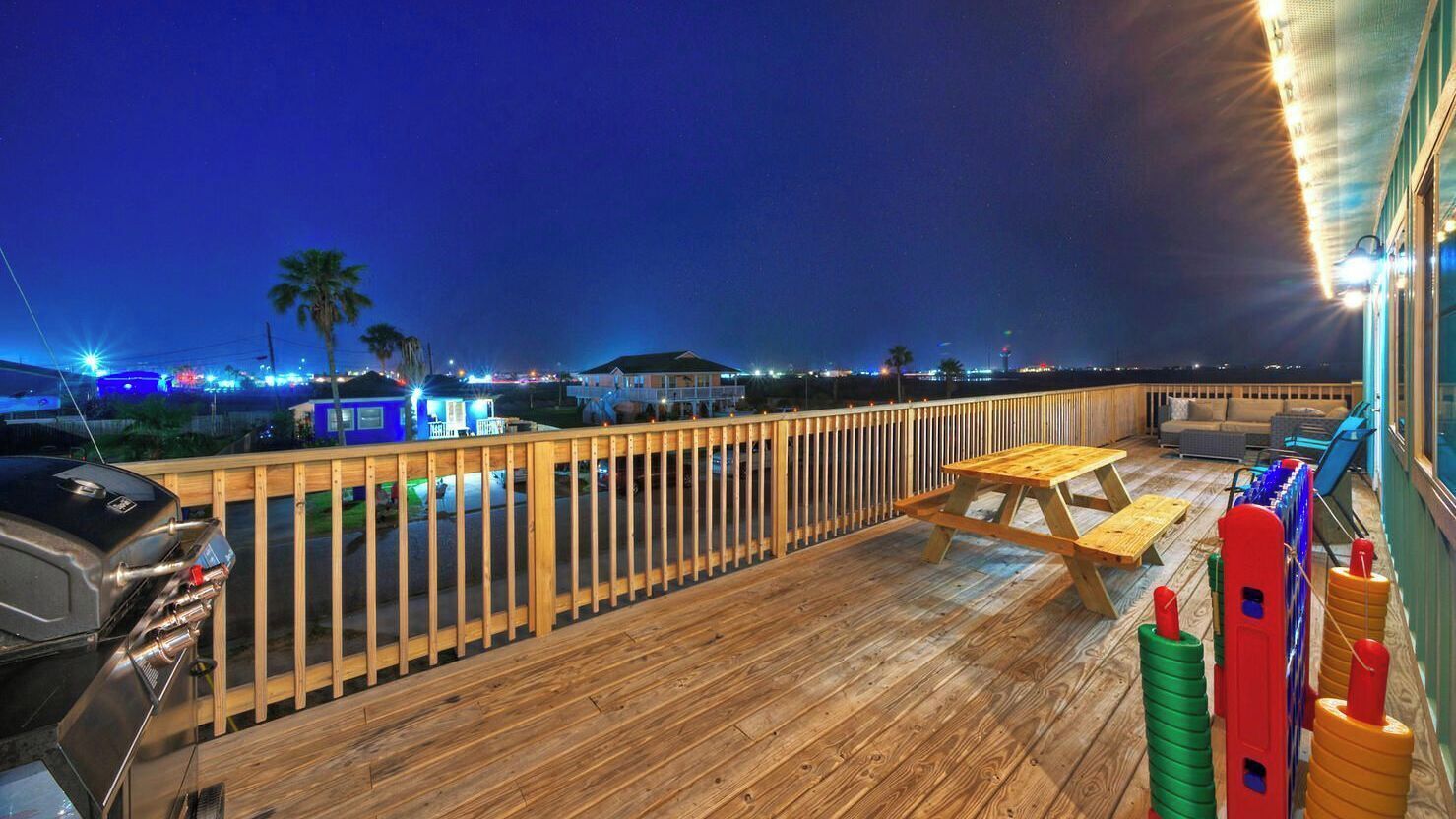 Une terrasse en bois avec un barbecue, une table de pique-nique et des bouteilles aux couleurs vives.